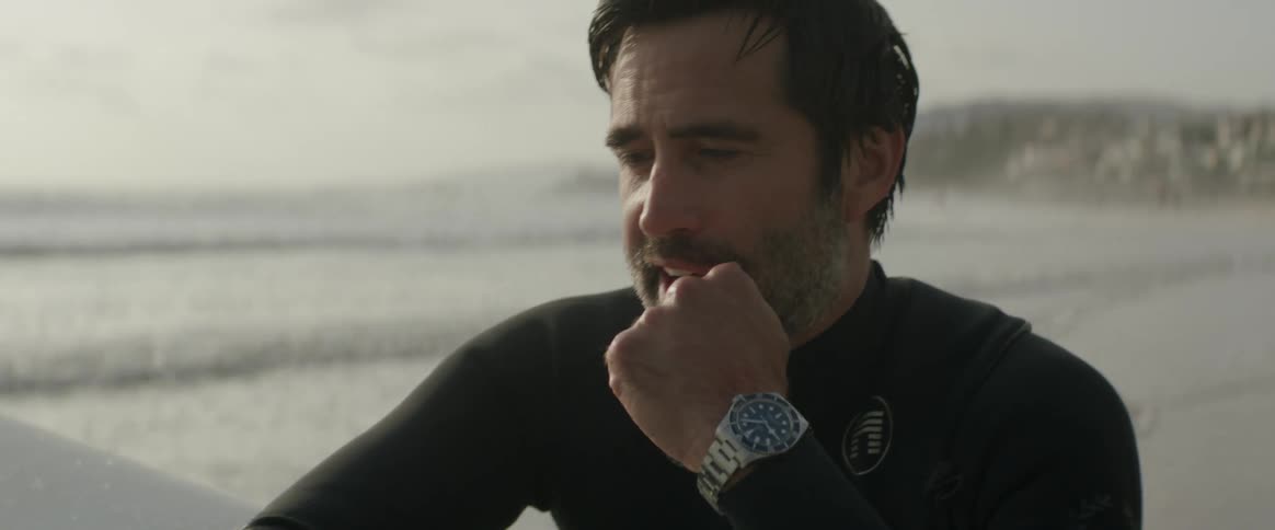 A man is standing on the beach with his surf board
