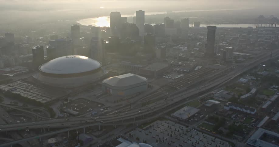 An atmospheric 4K aerial footage of a morning flyover of Downtown New Orleans with high-rise buildings skyscrapers and city river reveal towards the Mississippi River at sunrise during the summer with a hazy view of the waterways and nearby Hyatt Mercedes