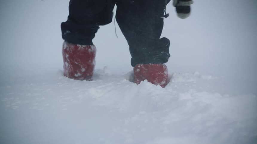 Close up of a mountaineer wearing red boots climb a hill covered in a thick layer of snow