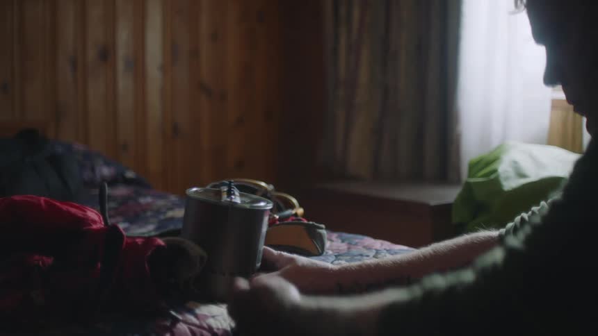 A person unpacks a bag and places gear on a bed in a room