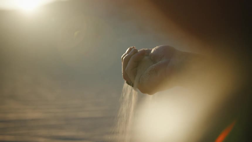 A man on the the desert letting a handful of sand fall through his fingers at sunset