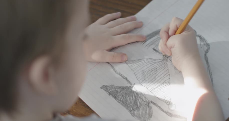 A young boy is drawing with a pencil on lined paper