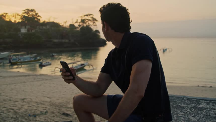 A man uses his phone on the beach