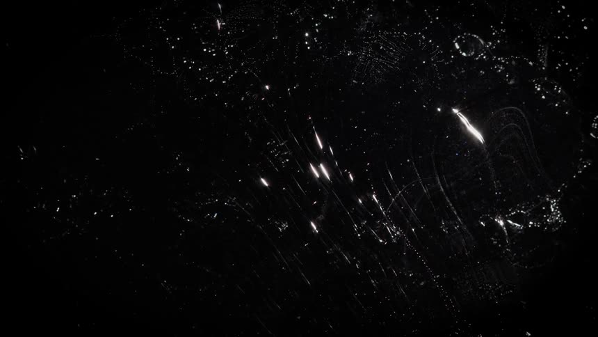 Clear fluid reflects light while flowing over whites spots on a black background
