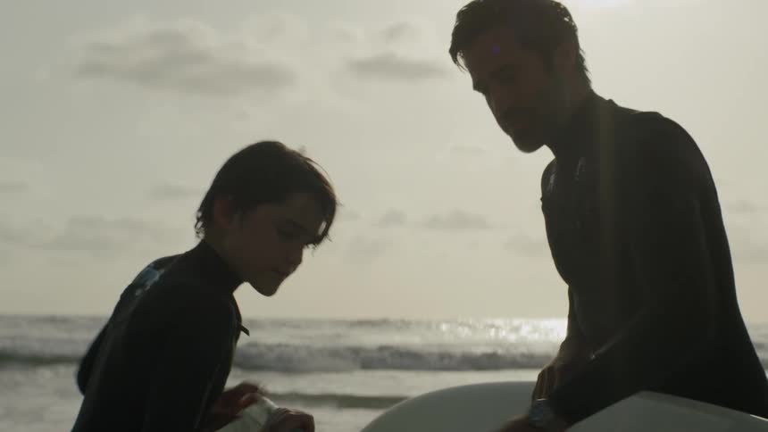 Father and son are looking at surfboards on a beach at the ocean