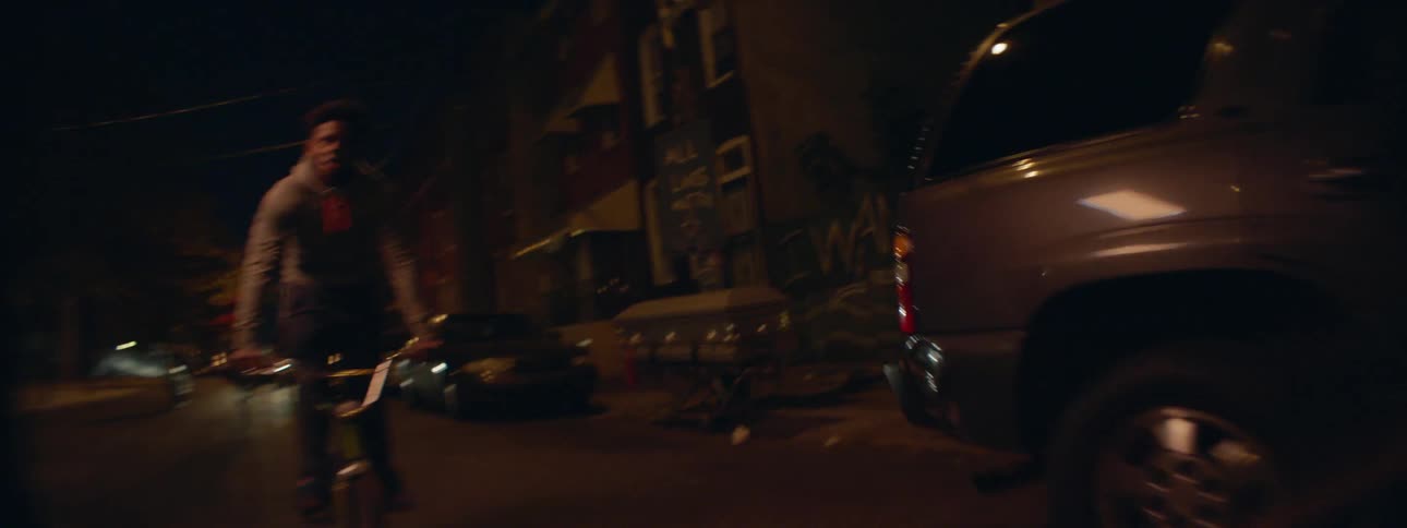 A group of kids ride down the street past a coffin