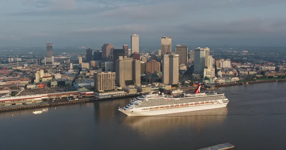 A Carnival cruise ship sails by Downtown New Orleans at sunrise giving an aerial view of the city’s skyscrapers and waterways