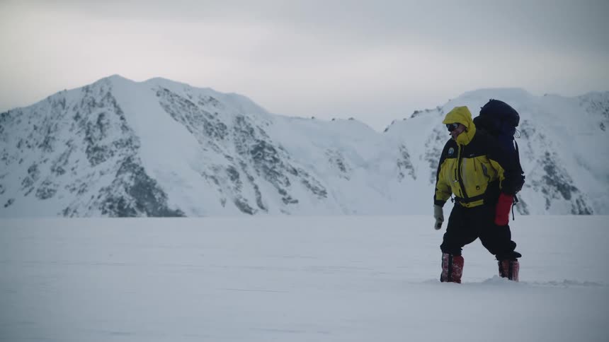 Mountaineer carrying a large backpack slowly walks over thick snow in the mountains