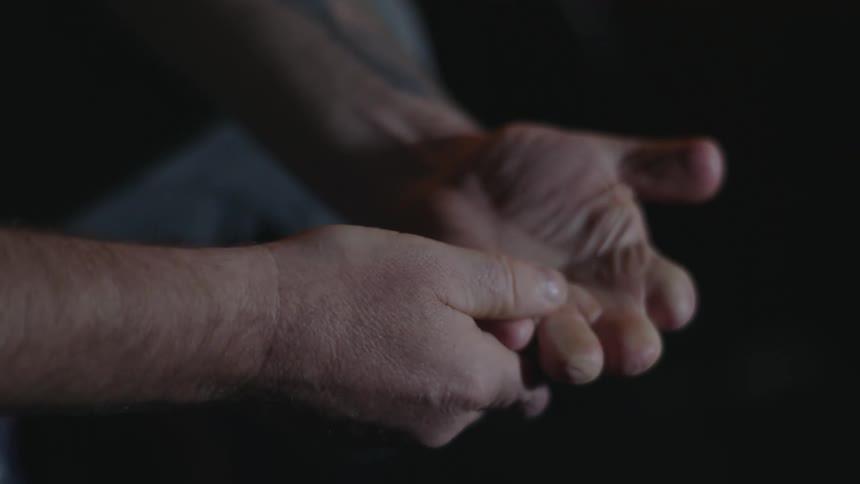 A close up of a mans face looking sad while looking at his hands