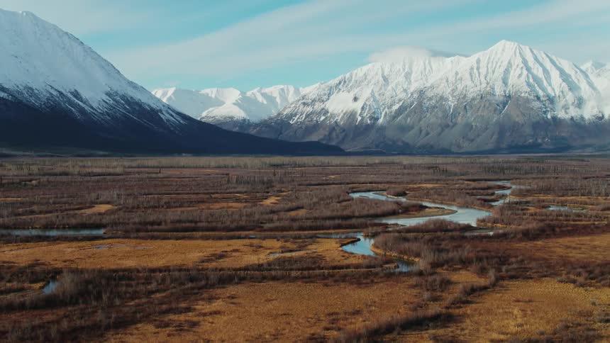 Snow capped mountains loom over the winding streams of a vast grassland during the day