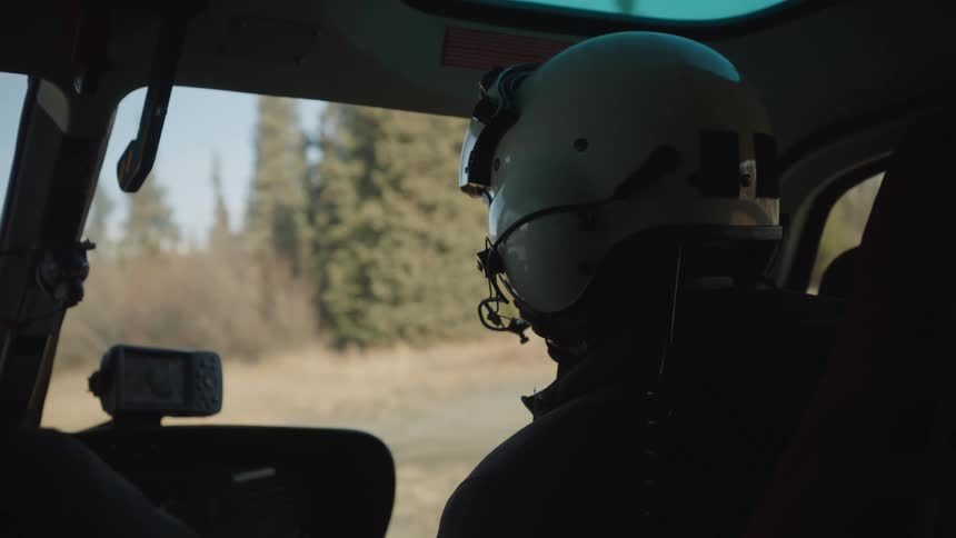 A man wearing a helmet piloting a helicopter that is on the ground