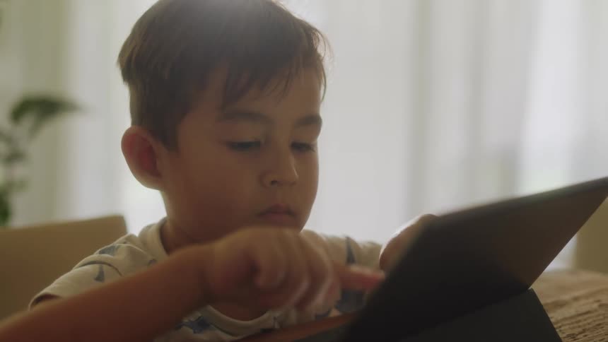 A boy looks down and types on his tablet while seated indoors