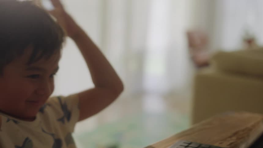 Boy with white t shirt uses tablet sitting at table in the living room at home