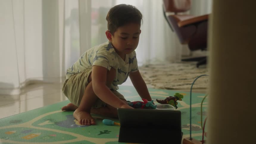 Boy with shirt and shorts uses tablet on the floor in the living room at home