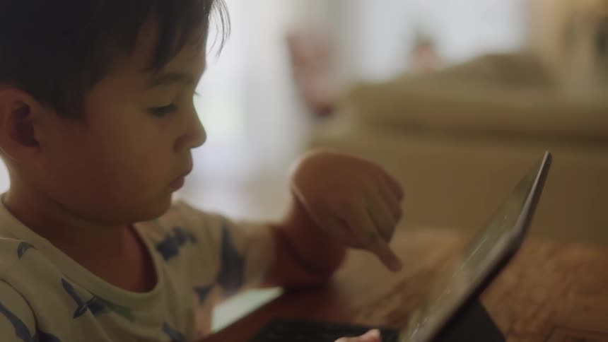 Close up of a boy playing a video game on a tablet in the living room at home