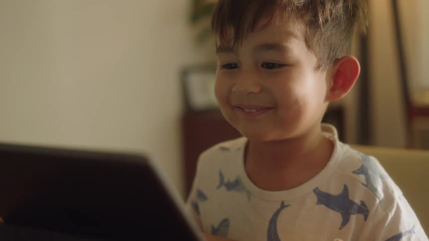 Close up of a boy playing a video game on a tablet in the living room at home