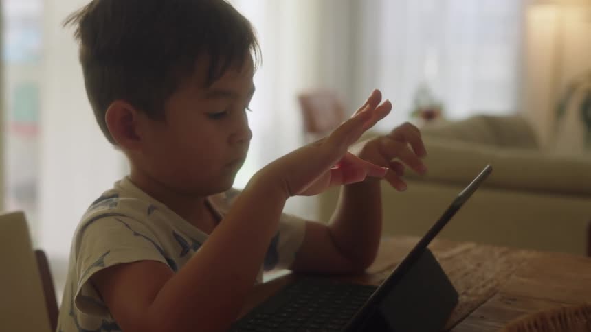 A boy touches a tablet while sitting at a table indoors