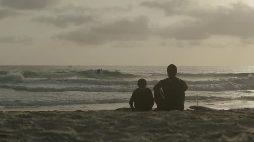 A man and boy sit together on a beach in the evening