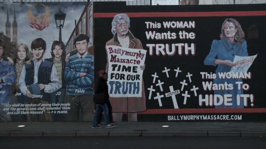 People walk by large murals on walls in a city
