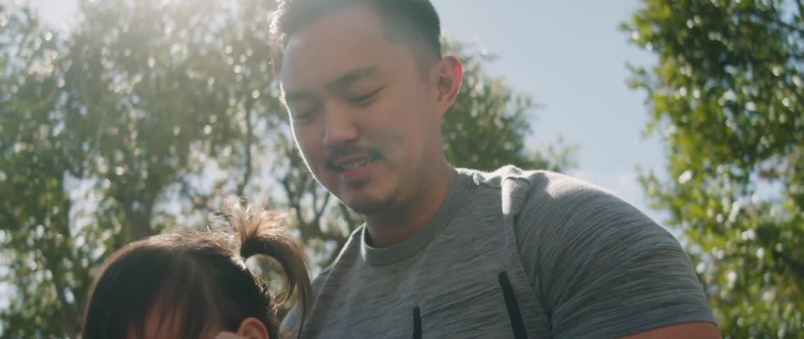 A father holds up his daughter playfully as they both smile and laugh