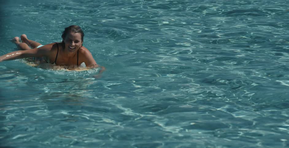 Woman smiling while paddling on surfboard in a swimming pool could be very clear seawater