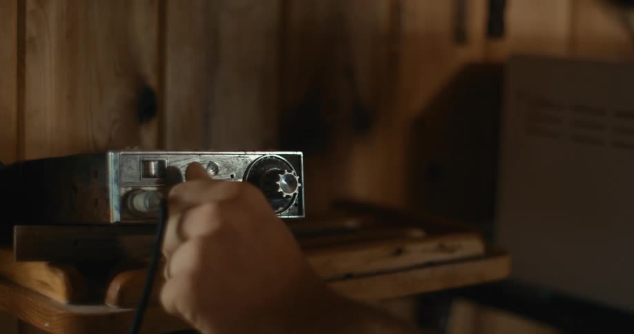 Close up of the hand of a person turning a knob on a vintage cb radio in a cabin