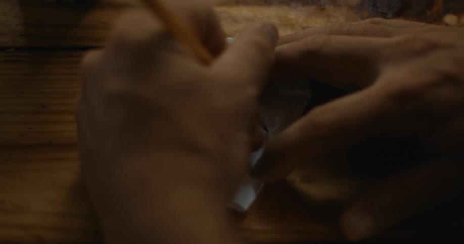 Person writes on piece of paper on wooden surface before taking paper away