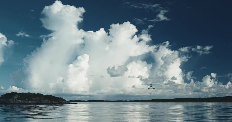 Seaplane flying overhead taking off over calm blue water into blue sky with fluffy clouds