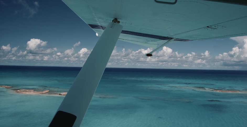 View from an airplane flying over the clear blue water and clouds on the horizon