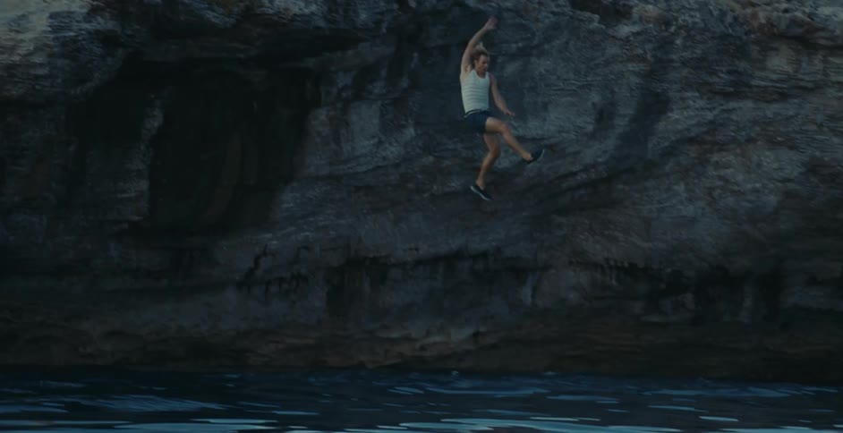A man is running across the top of a promontory and he runs over the edge into the water