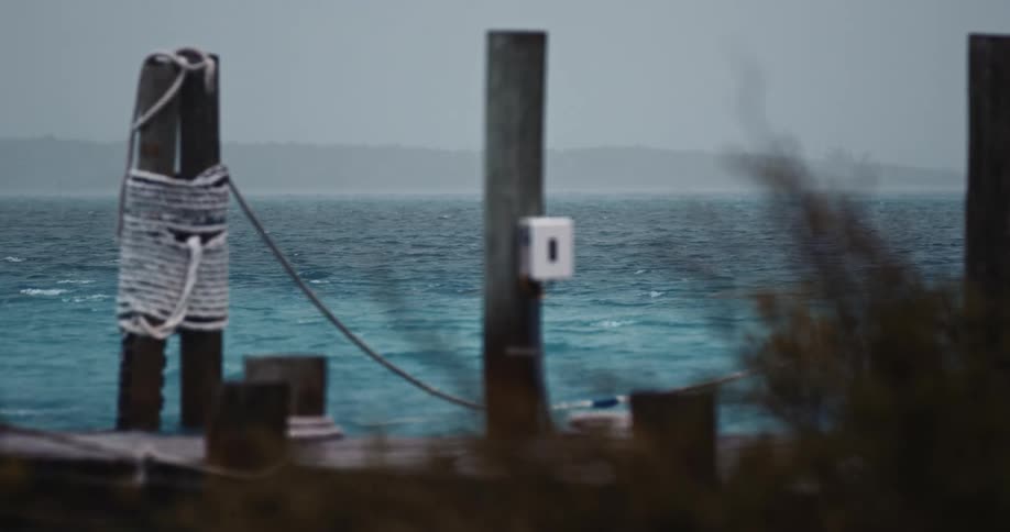 A wooden dock pier with rope tied around the poles and the ocean waves ripple behind