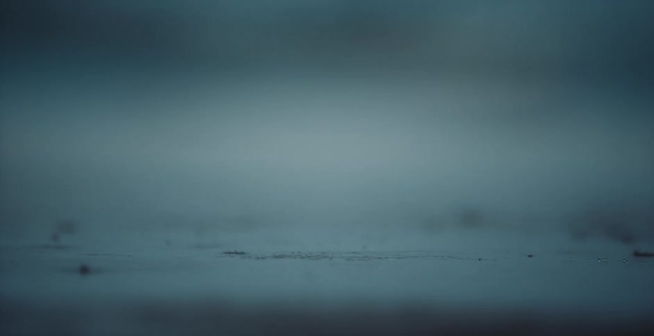 Rain falls onto surface creating small splashes as the drops hit