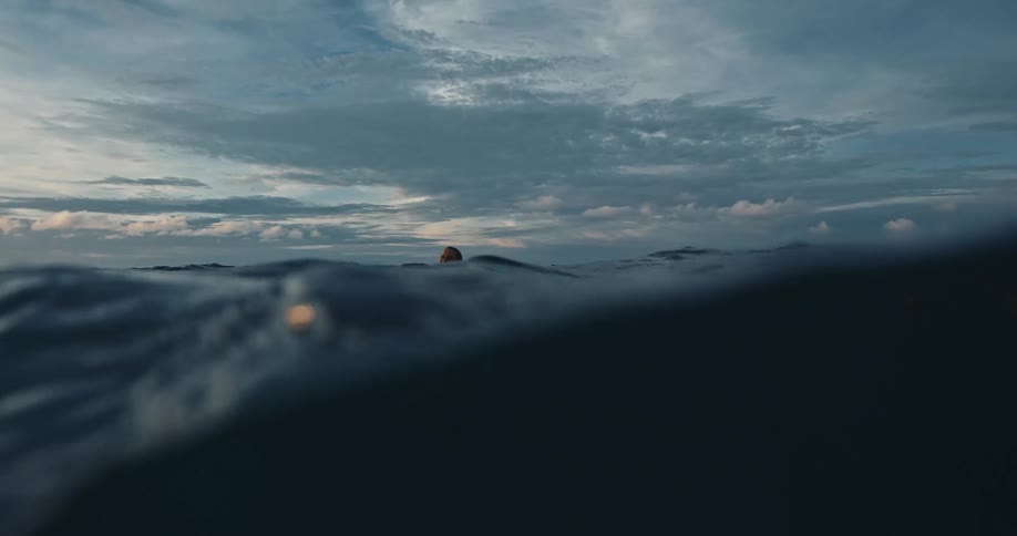 A man is swimming in rough water as his head sticks out among the waves under a cloudy sky