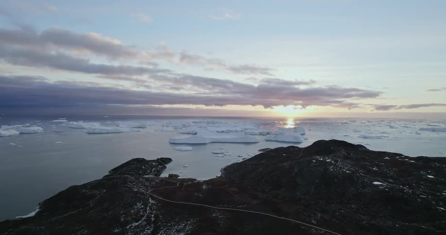 Aerial view of the sun setting over icebergs floating on the arctic ocean at morning