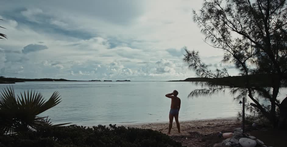 A man is standing on the beach and drinking a beverage