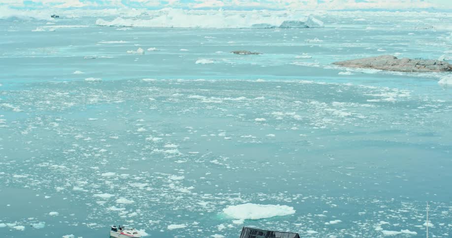 An aerial of a house on rocks near an ocean with ice in it