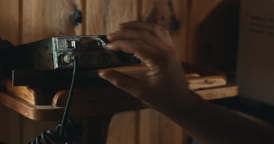 Man adjusts dial on cb radio sitting on shelf against wooden wall
