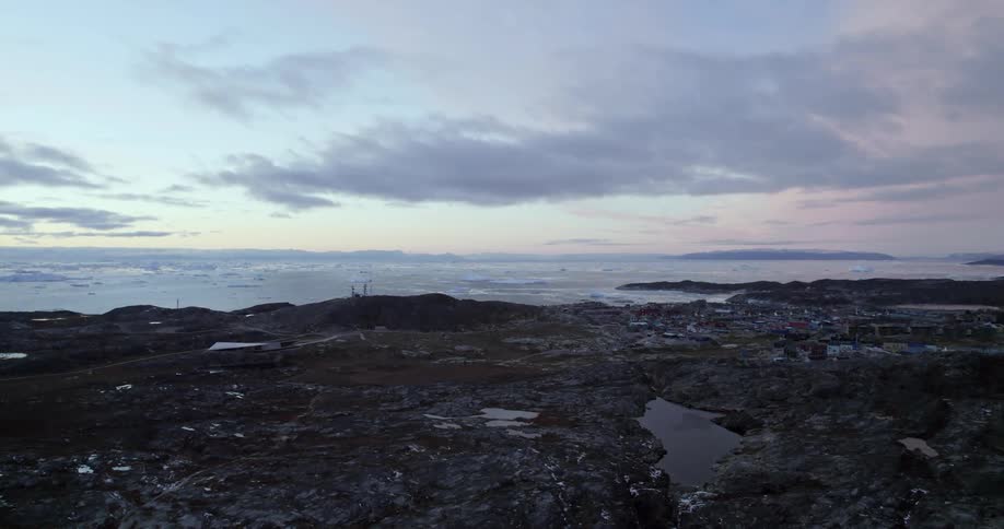 Ice floats in sea near coastal town under a cloudy sky