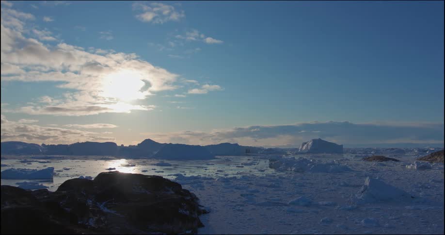 Sun shines brightly through cloud and is reflected by ice filled water near coast