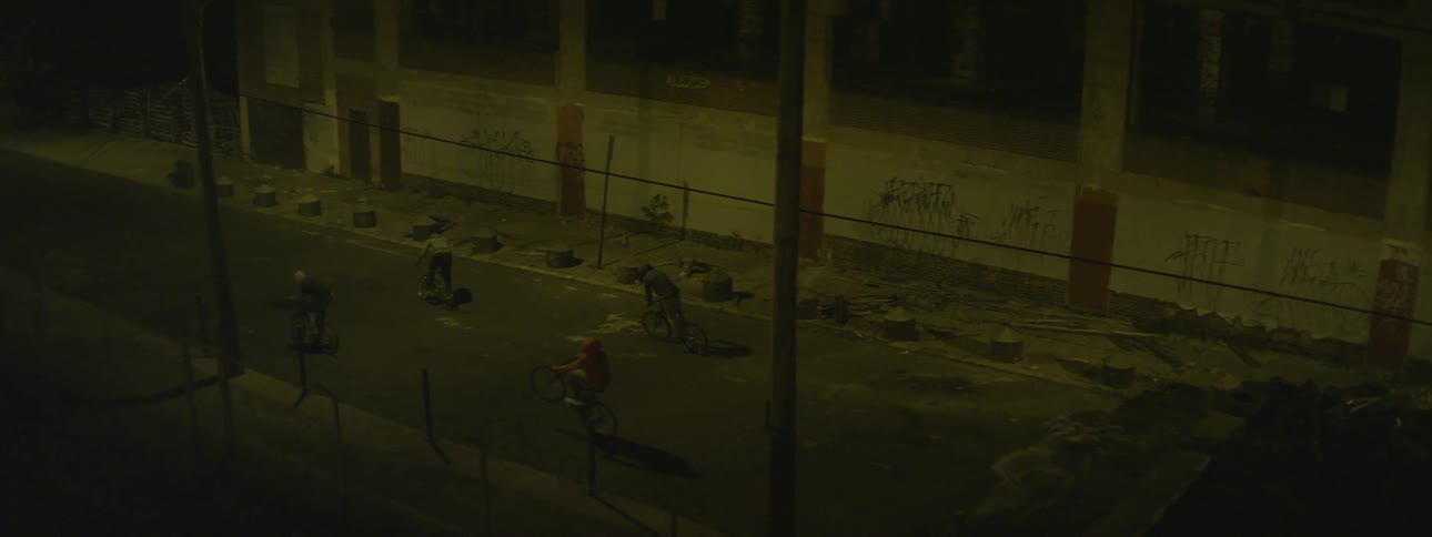 A group of boys ride their bikes down a dark road