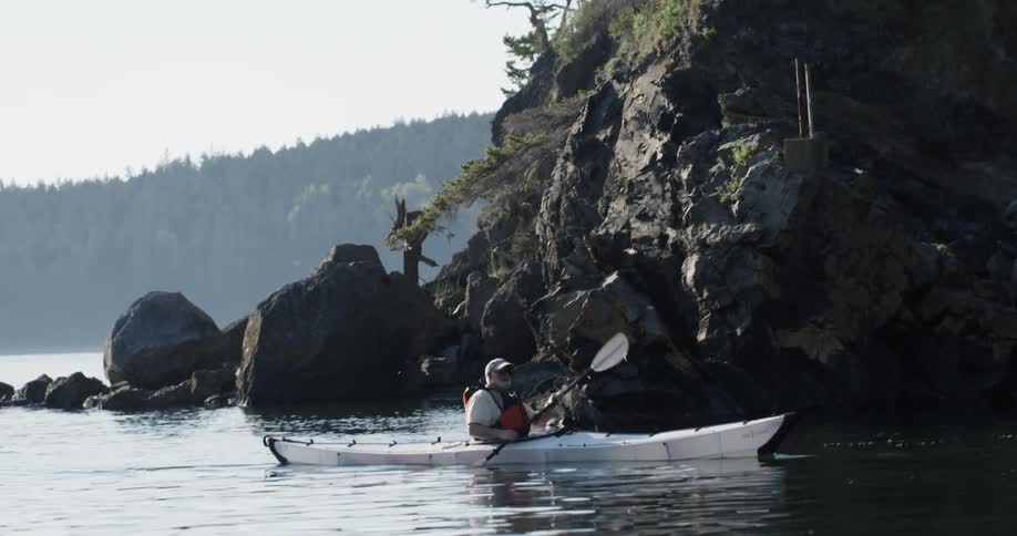 A man kayaks near a rocky shore