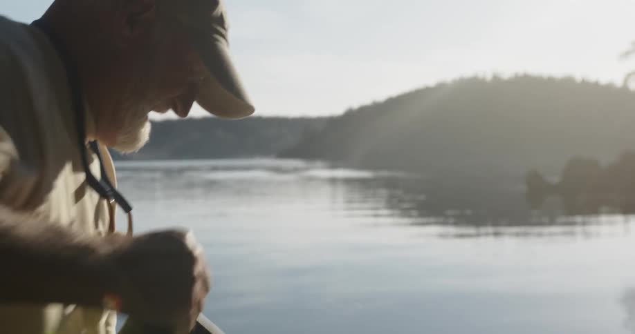 An older man halls a heavy sack near some kayaks on the shore of a body of water