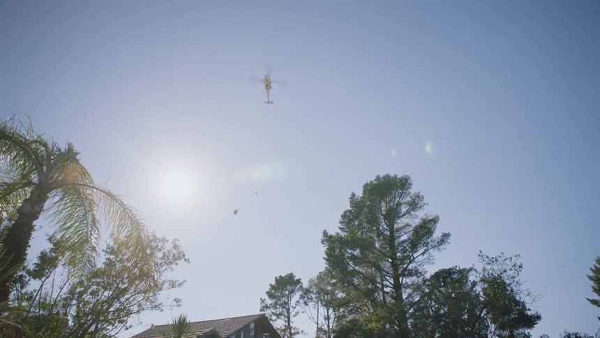 Helicopter hovering in the sky above residential area with the sun behind it