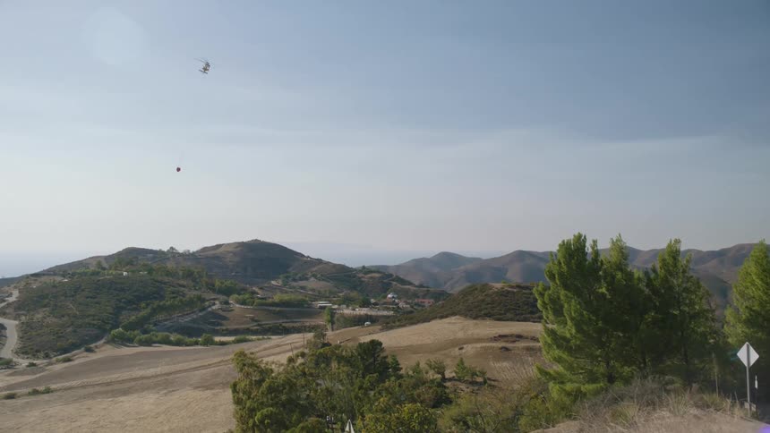 A helicopter flies over the deserted plains and canyons before green mountain peaks