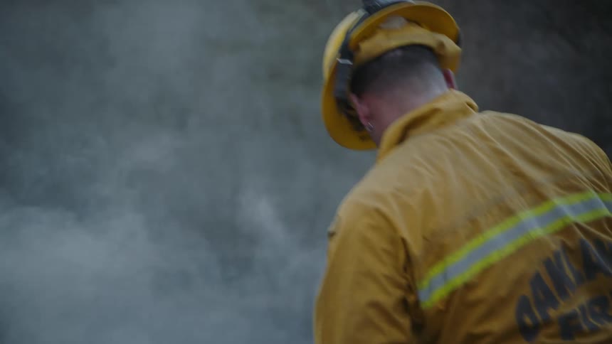 A fireman is moving a large smoldering rock while helping to fight a forest fire in the daytime