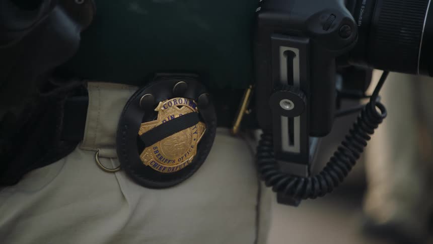 A close up of a persons badge on their belt next to a camera on the persons waist