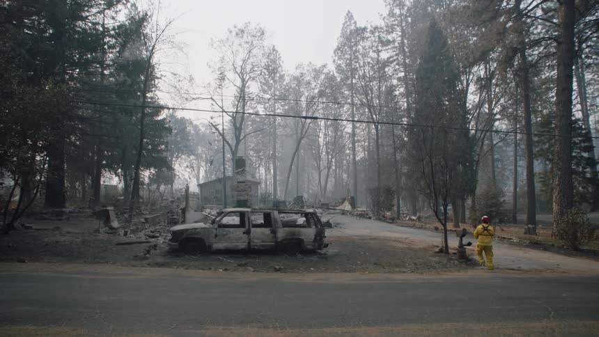 A firefighter walking down the street near a burnt car putting a ribbon on the mailbox