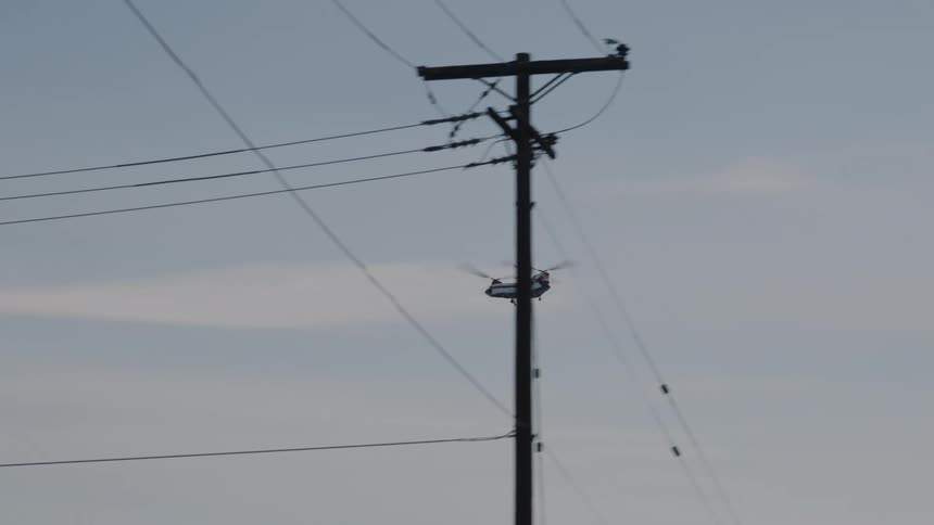 A transport helicopter flies into the distance past a telephone pole and metal fence