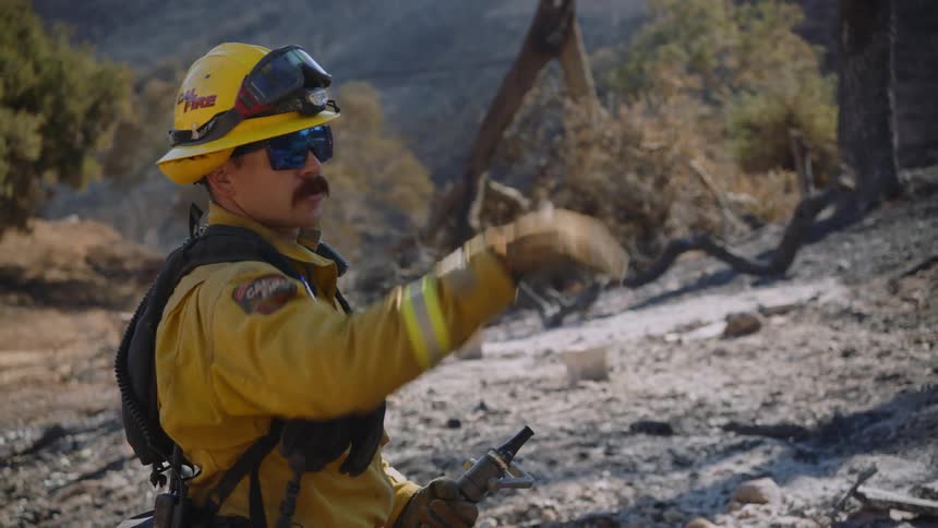 Firefighters wearing yellow protective gear pointing up the hill of a burned area in the mountains