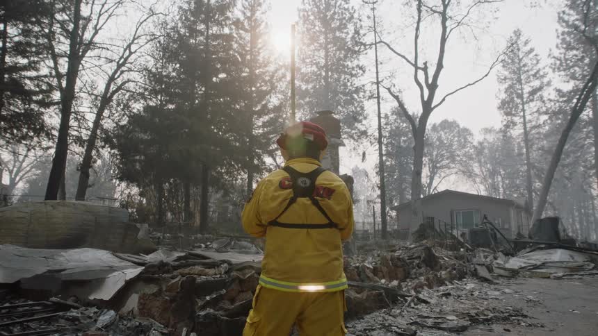 The backside of a firefighter standing looking at fire debris and ashes of a home